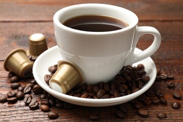 Coffee capsules, cup of hot drink and beans on wooden table, closeup