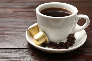 Coffee capsules, cup of hot drink and beans on wooden table, closeup