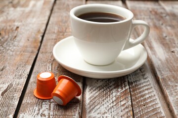 Coffee capsules and cup of hot drink on wooden table, closeup