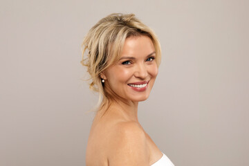 Fototapeta premium Closeup Portrait Of Smiling Attractive Middle Aged Woman With Bare Shoulders Posing Over Grey Studio Background, Happy Mature Lady With Beautiful Aged Skin Looking At Camera, Copy Space. High quality
