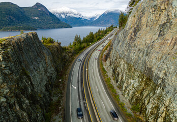Scenic Mountain Highway with Cars Overlooking a Tranquil Lake Under Snow-Capped Peaks