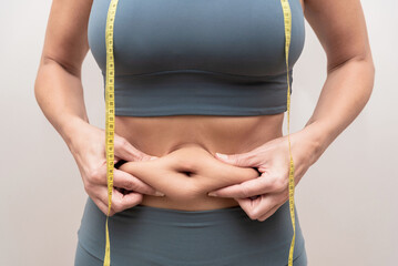 close up of Woman pinching belly fat with a yellow measuring tape around waist