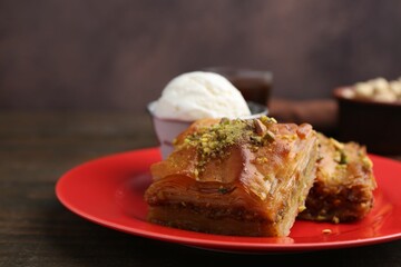 Tasty baklava with chopped nuts and scoop of ice cream on wooden table, closeup