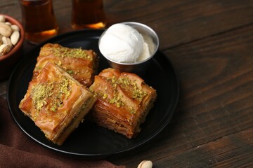 Delicious baklava with crushed nuts and ice cream served on wooden table, closeup. Space for text