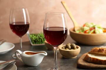 Red wine and delicious dinner served on grey table, closeup