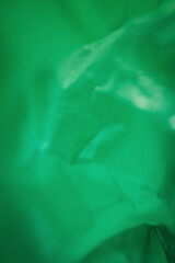 Extreme close up of green empty plastic bag background. The plastic surface is wrinkly and tattered making abstract pattern. Selective focus, shallow depth of field.