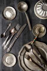 Vintage pewter plates, bowls and cutlery on black chalkboard background. Flat lay. Top view. Food...