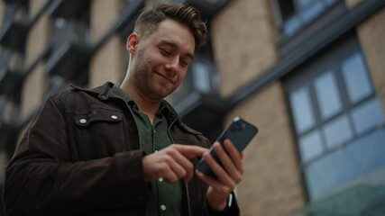 Low-angle view of concentrated young male navigating digital content, networking through mobile device. Close-up of cheerful man checking smartphone standing on urban street. Shooting in slow motion. - Powered by Adobe