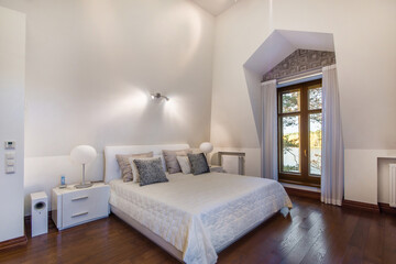 Fototapeta premium The interior of a bedroom in a luxurious country mansion with a beautiful view of the .lake from the window. White room decor, parquet floor.