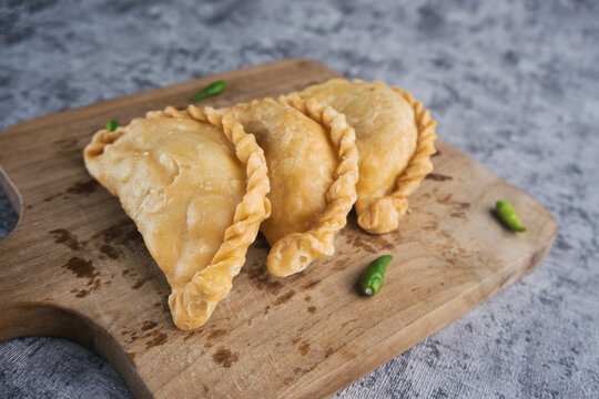 Kue Pastel or Jalangkote, Indonesian traditional snack filled with carrot and potatoes served On Wooden Cutting Board With Fresh Green Chilis