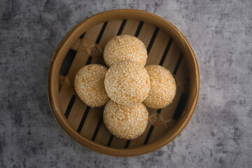 Traditional Sesame Ball Pastries in Bamboo Steamer on Textured Background