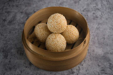 Traditional Sesame Ball Pastries in Bamboo Steamer on Textured Background
