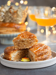 Close up of tradition French galette des rois or king's cake with its fève inside, cut piece with crown and glasses of cider in background. A cake  usually served on Epiphany. Cake made puff pastry.