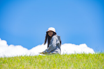 Young Asian woman walking on a green hill, smiling at the camera, against a blue sky