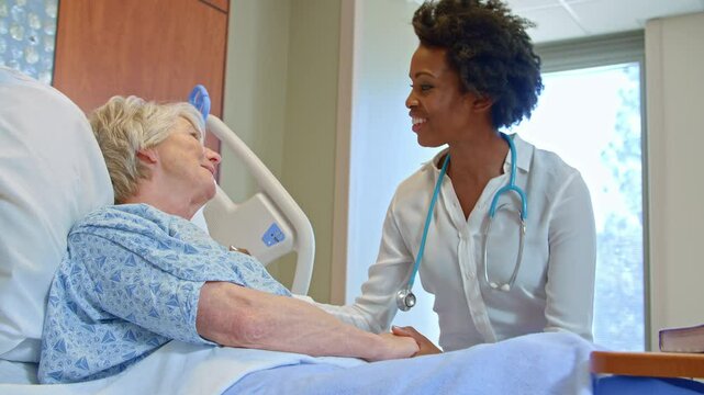 Handheld shot of doctor wearing visiting senior female patient lying in hospital bed giving her good news  - shot in slow motion
