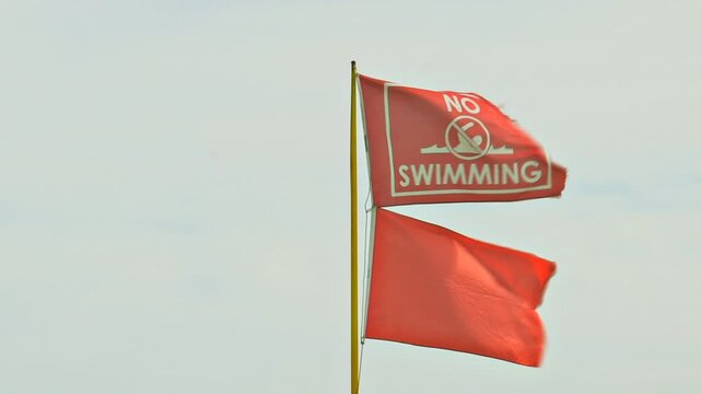 Close up of beach warning flags, the red flag, indicating high hazard/ and or strong currents blows in the breeze with a red "no swimming" flag.