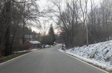 A winding road through a serene forest landscape with bare trees and a hint of snow, evoking a peaceful winter atmosphere.