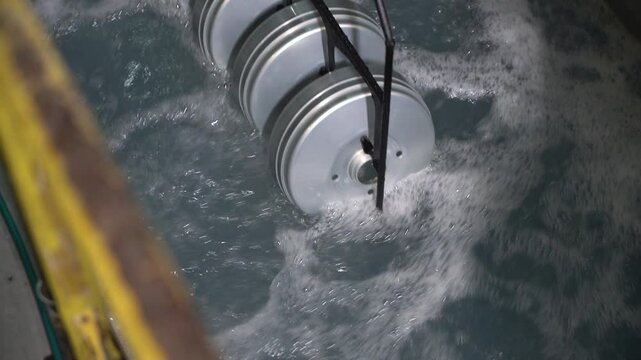 Close up view of dipping hanged metal pieces in the electropaint tank for the cataphoresis or paint process on the automated conveyor in a factory.