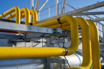 Supply of industrial gas yellow piping with dew drops on racks over roof of manufacturing plant during sunny spring day