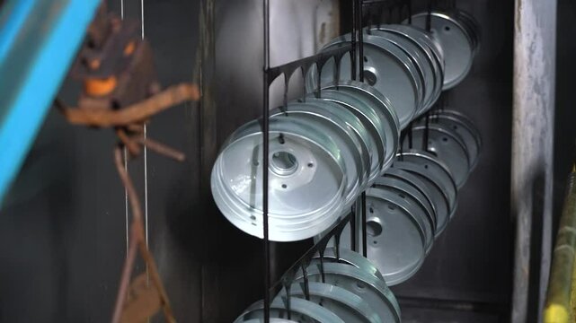 Close up view of dipping hanged metal pieces in the electropaint tank for the cataphoresis or paint process on the automated conveyor in a factory.