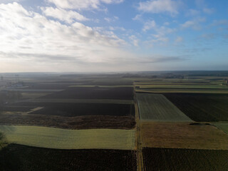 Aerial view of agricultural fields with varying shades of green and brown. The sky is partly...