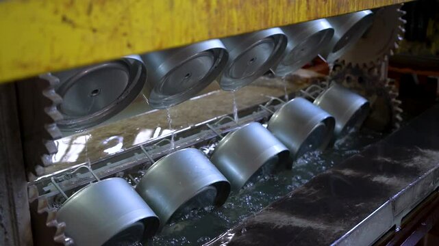 Close up view of dipping hanged metal pieces in the electropaint tank for the cataphoresis or paint process on the automated conveyor in a factory.
