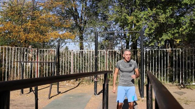 54-Year-Old Fit Man Doing Parallel Bar Dips - Sunny Day. Front view captures muscle contractions, visible effort on his face and rhythmic breathing. Suitable for strength and endurance training.