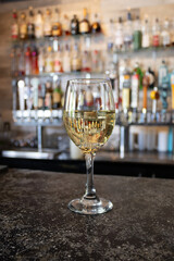 Glass of white wine on bar counter with liquor bottles and taps in the background