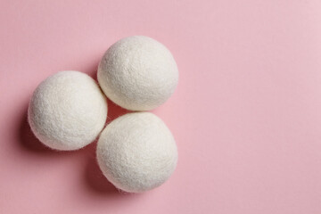 Trio of white wool dryer balls arranged in a triangle on a pastel pink background. Soft wool texture and eco-friendly design highlight sustainable laundry care