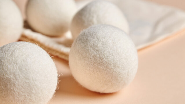 Close-up of white wool dryer balls beside a cotton bag on a beige background. Eco-friendly, reusable laundry solution for reducing static and drying time