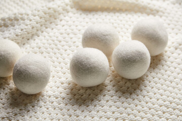 White wool dryer balls arranged on a soft, textured knitted surface, conveying an eco-friendly and cozy vibe. Perfect for showcasing natural laundry essentials