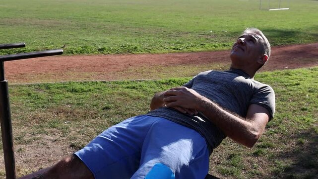 54-Year-Old Fit Man in Excellent Physical Condition Doing Crunches on Parallel Bars. Shot from above captures effort on his face. Suitable for fitness promotion and showcasing challenging exercises.