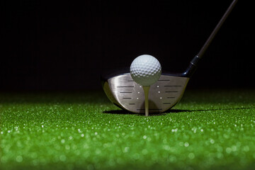 Low angle selective focus of golf ball and driver on a green with black background