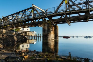 Serene view of a steel bridge over calm waters with boats in the distance