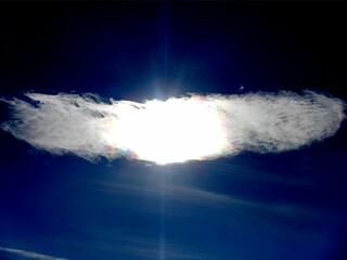 Dark blue sky, sun rays and colorful, pearl colors on Clouds iridescence, Irisation around sun - abstract sky background. Topics: optical phenomenon, beauty of nature, air space, weather, meteorology