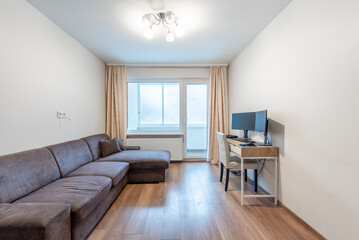 Modern Home Living Room Interior With Sofa and Wooden Floor Featuring Home Office Setup. Door to Balcony, Windows and Curtains