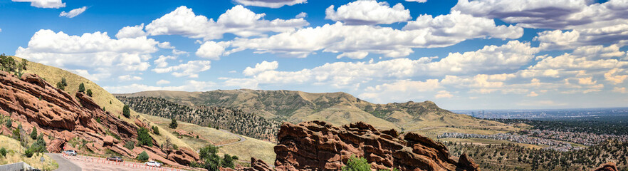 Experience the breathtaking panoramic beauty of Red Rocks, Colorado, with panoramic views of Denver. Rugged red cliffs, blue skies, and puffy white clouds create a stunning natural backdrop.