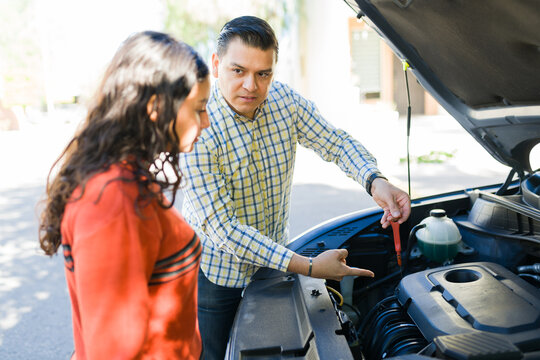 Latin dad showing his teen daughter how to check the oil level in a car engine