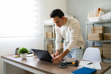 Small ecommerce business owner managing laptop and preparing packages for delivery in his small...