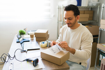 Male entrepreneur in a small business startup office placing a shipping label on a cardboard box
