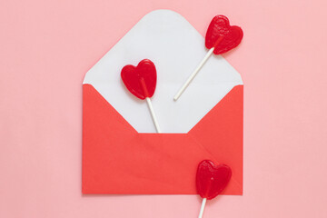 Red envelope with valentine's day love letter on pink background with red heart lollipops