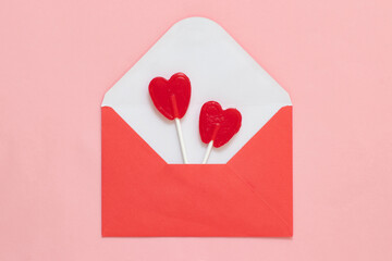 Red envelope with valentine's day love letter on pink background with red heart lollipops