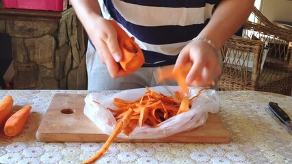 Person is cutting carrots on a wooden cutting board. The carrots are in a plastic bag and the person is using a knife to cut them