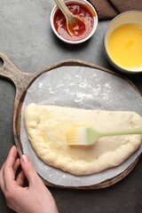 Woman brushing egg yolk on calzone pizza at grey table, top view