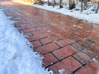 An icy pedestrian path sidewalk in winter with snow and sand