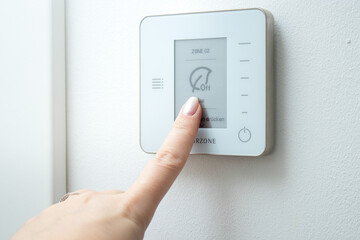 Close up of female finger touching a modern thermostat control system on white wall 