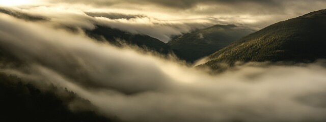 A moody photograph of a dense fog rolling over a mountain pass at sunrise, Mountain fog scene, Moody style