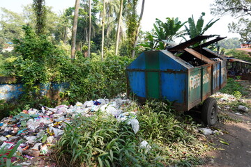 waste bin overflowing with garbage, with some of the rubbish spilling onto the ground with trees...