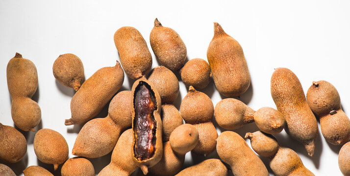 Tamarind tropical fruits isolated on white background. Fresh ripe dryed Tamarind fruits (Tamarindus indica, Indian date) border design, healthy vegan food. Top view, flat lay