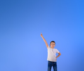 Portrait of confident boy pointing up at copy space for advertisement while standing on blue background